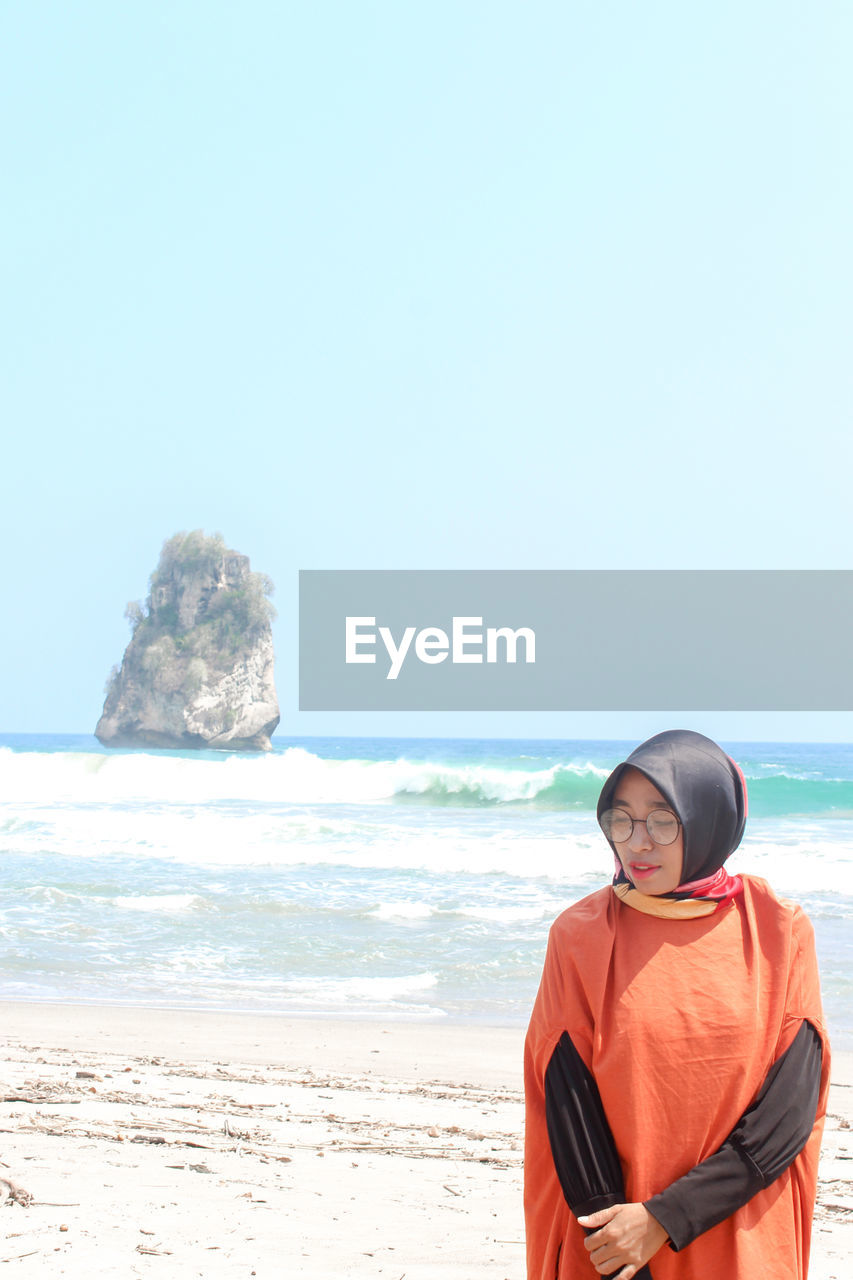 Woman in hijab standing at beach against clear sky