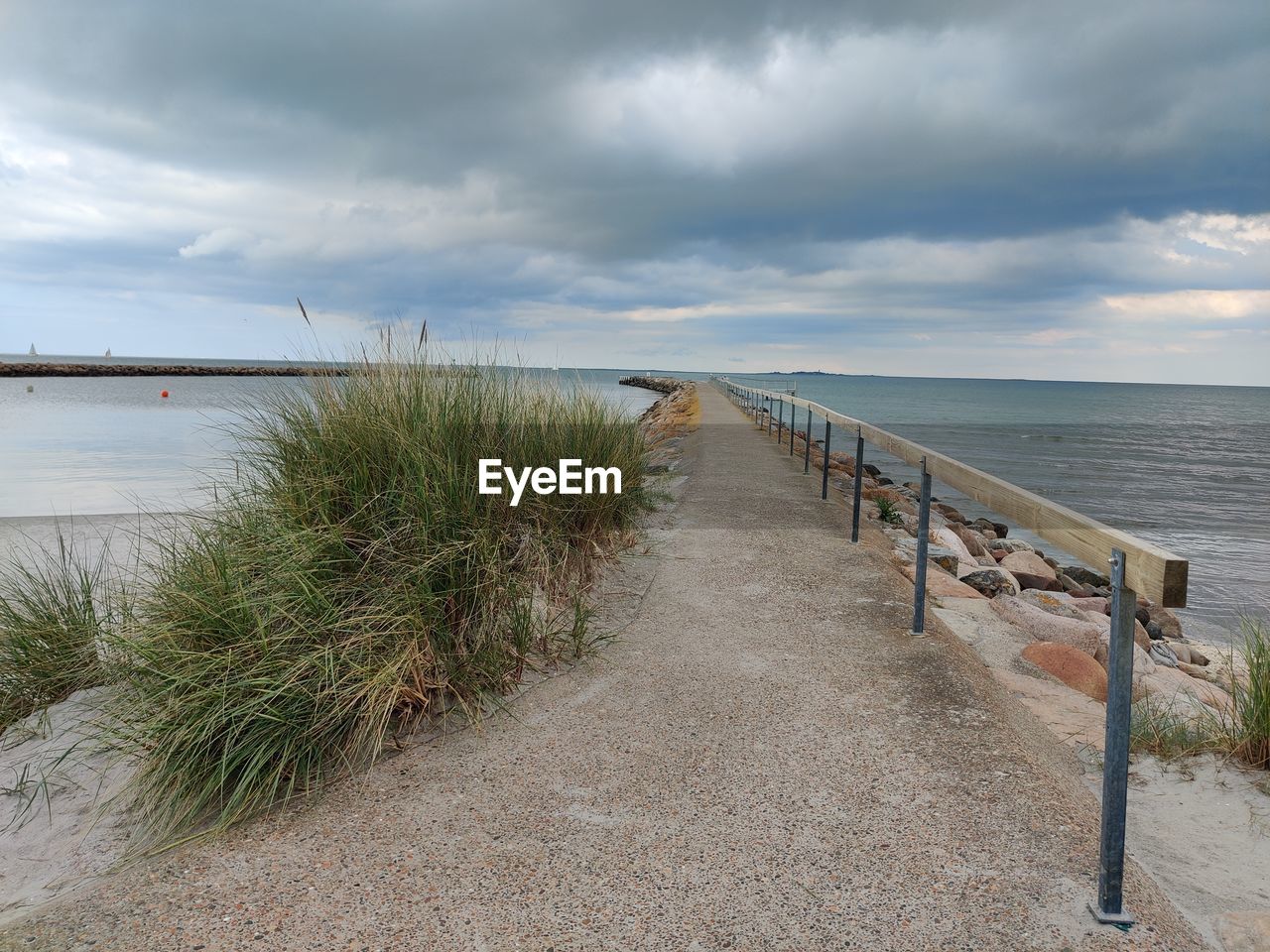 water, sky, sea, beach, cloud, shore, land, coast, nature, sand, scenics - nature, beauty in nature, walkway, horizon over water, tranquility, ocean, horizon, tranquil scene, plant, coastline, environment, no people, landscape, overcast, footpath, sand dune, grass, holiday, day, travel destinations, outdoors, seascape, non-urban scene, bay, trip, travel, vacation, marram grass, body of water, tourism, architecture, dramatic sky, the way forward, cloudscape, idyllic, storm, boardwalk, water's edge, absence, coastal feature, wood, railing, pier