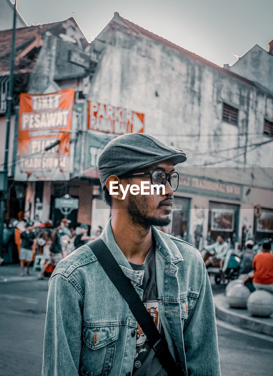 PORTRAIT OF MAN STANDING ON STREET AGAINST CITY