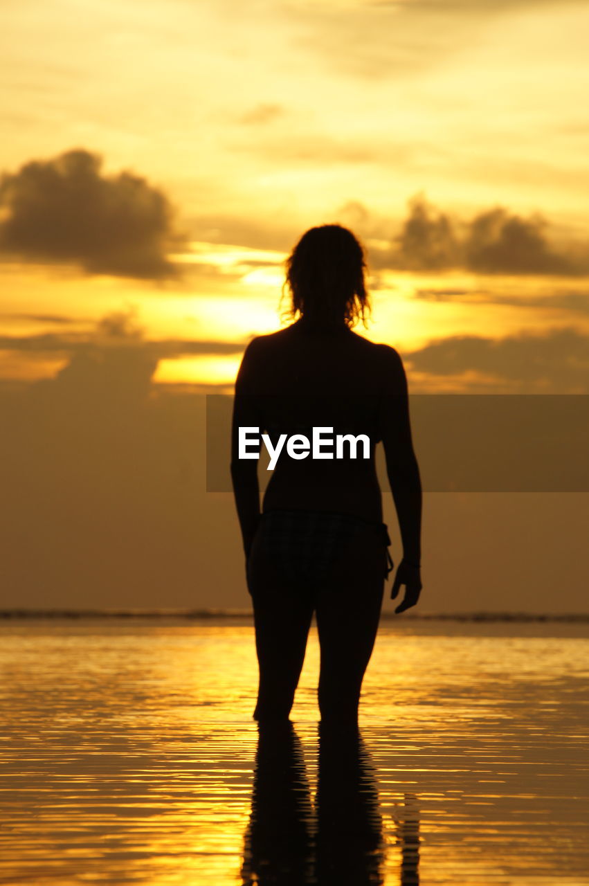 Rear view of silhouette woman standing at beach during sunset