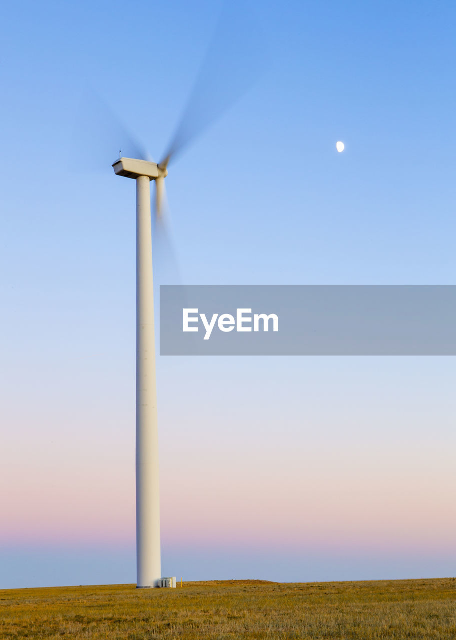 Wind turbine in motion against blue sky with moon