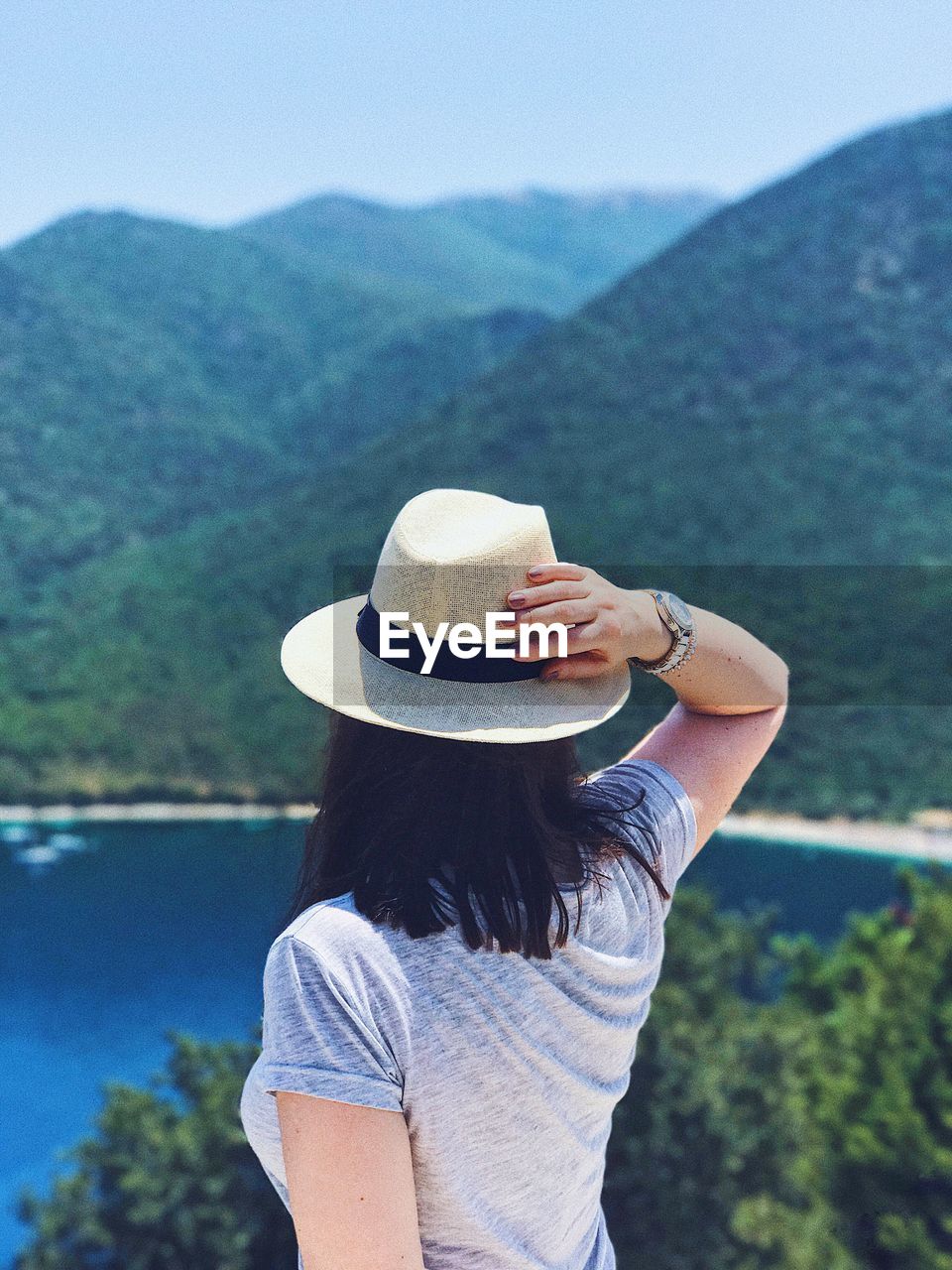 REAR VIEW OF WOMAN WITH HAT STANDING AGAINST MOUNTAIN