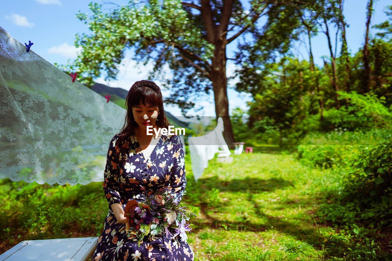 Woman holding bouquet while sitting in park