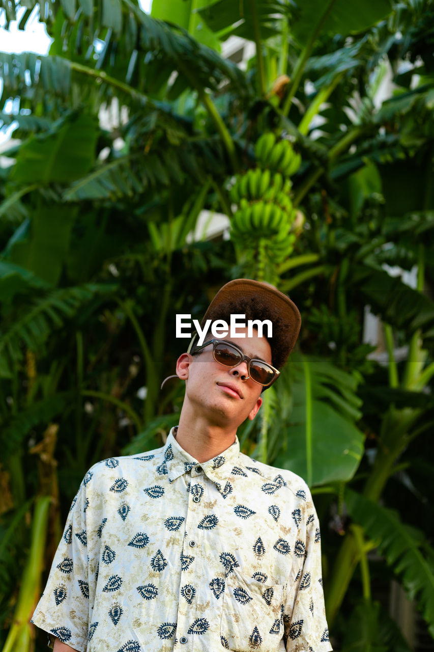 A young guy wearing summer clothing. palm tree as background.