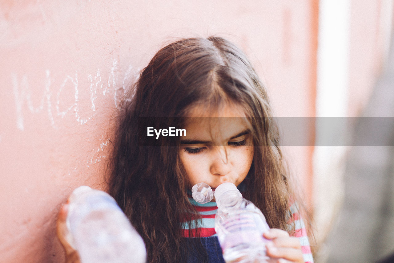 Girl drinking water while leaning on wall