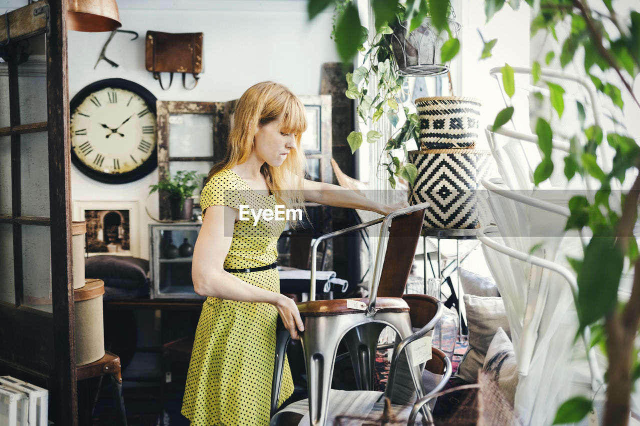 Mid adult woman stacking chairs in interior design shop