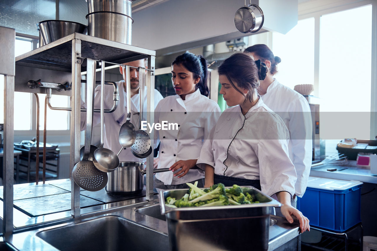 Chef team looking at colleague cooking food in commercial kitchen