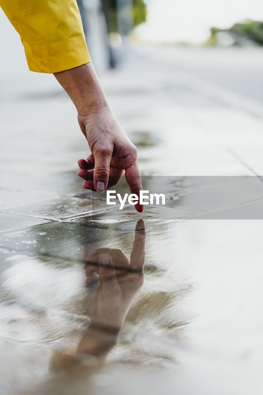 Woman' hand touching rain puddle on street