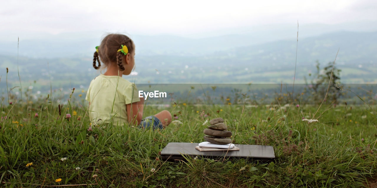 Cute girl relaxes in the mountains. stack of zen stones and digital gadget, laptop and mobile phones