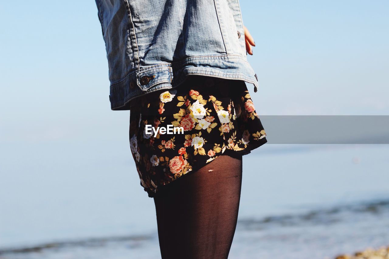 Midsection of woman standing at beach against sky