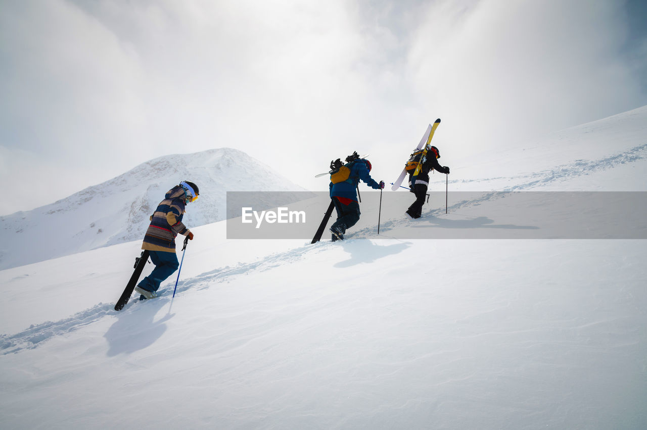 Three friends snowboarders skiers go uphill with a snowboard and skis in their hands for backcountry