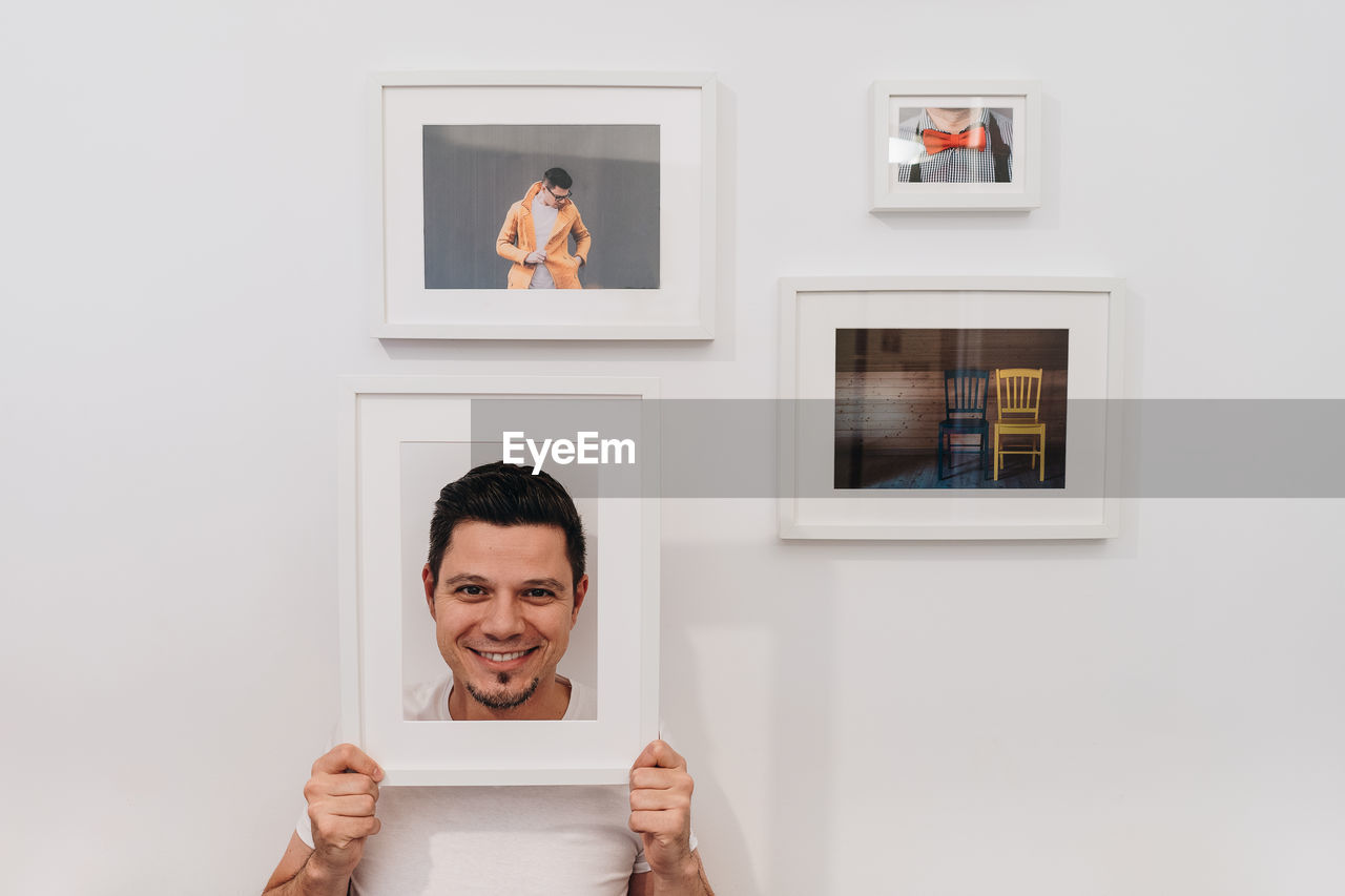 Portrait of man holding frame against wall