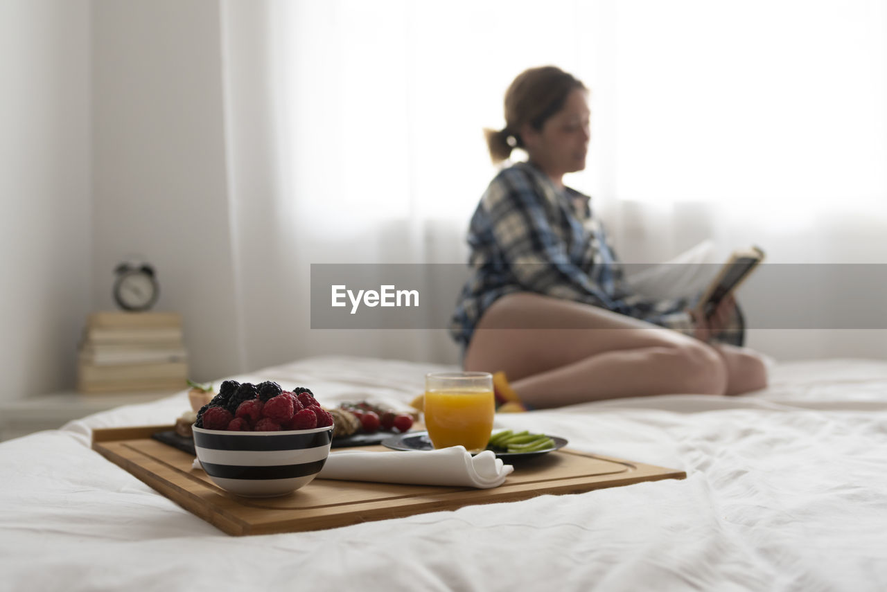 Focused breakfast tray and unfocused woman reading on background.