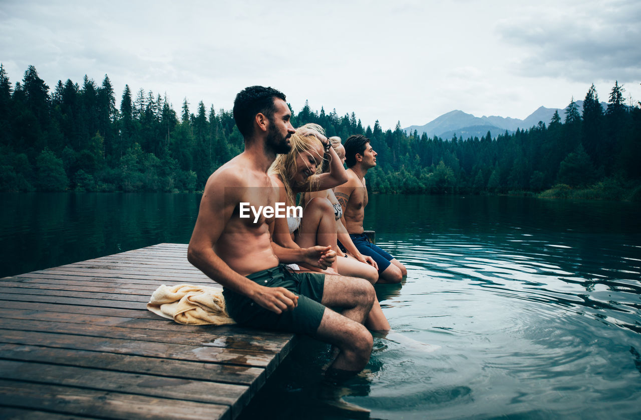 YOUNG MEN SITTING ON LAKE AGAINST SKY