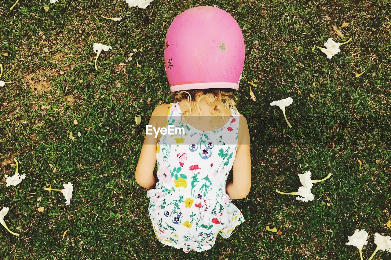 Rear view of girl wearing pink helmet while bending on grassy field