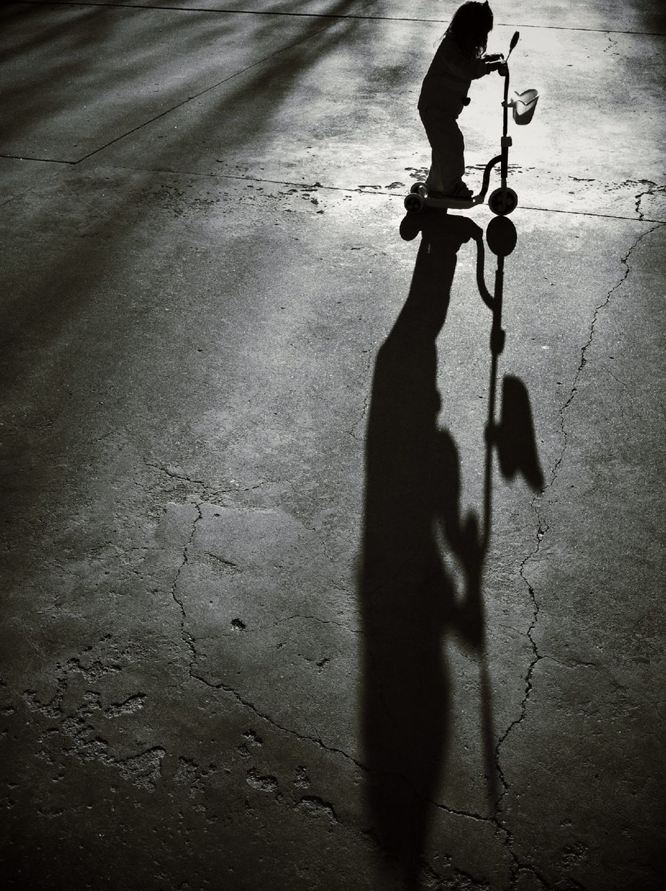 Girl with shadow riding tricycle on road