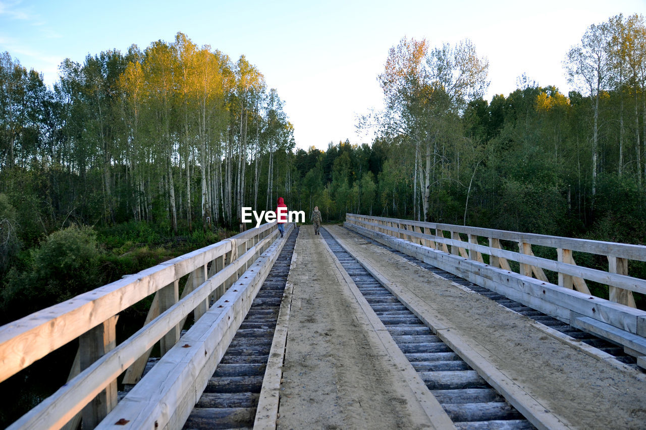 People on footbridge leading towards forest