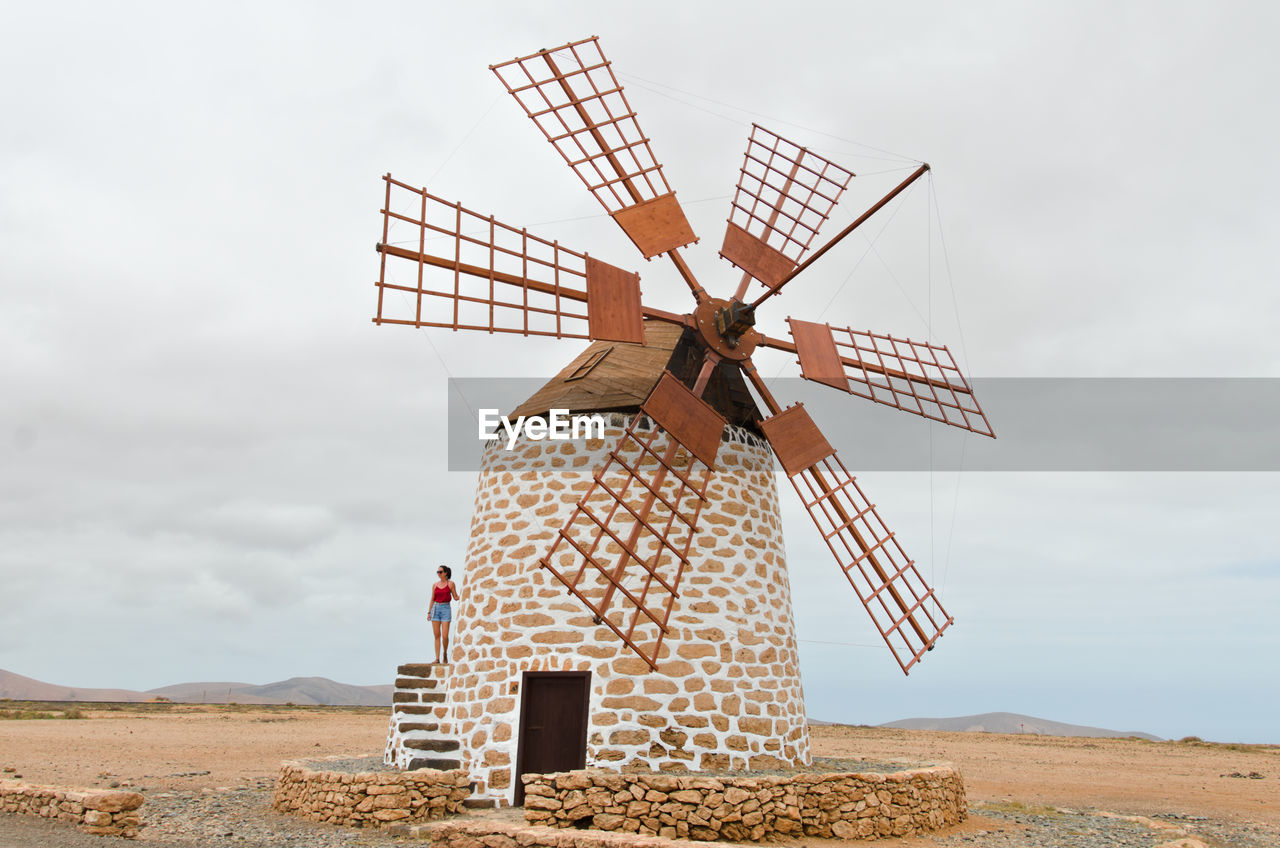 Woman standing on traditional windmill against sky