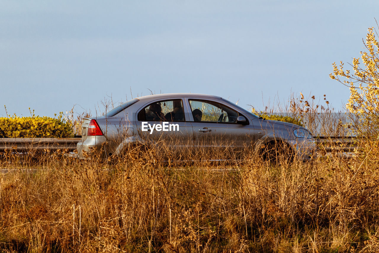 VIEW OF ABANDONED CAR ON FIELD AGAINST CLEAR SKY