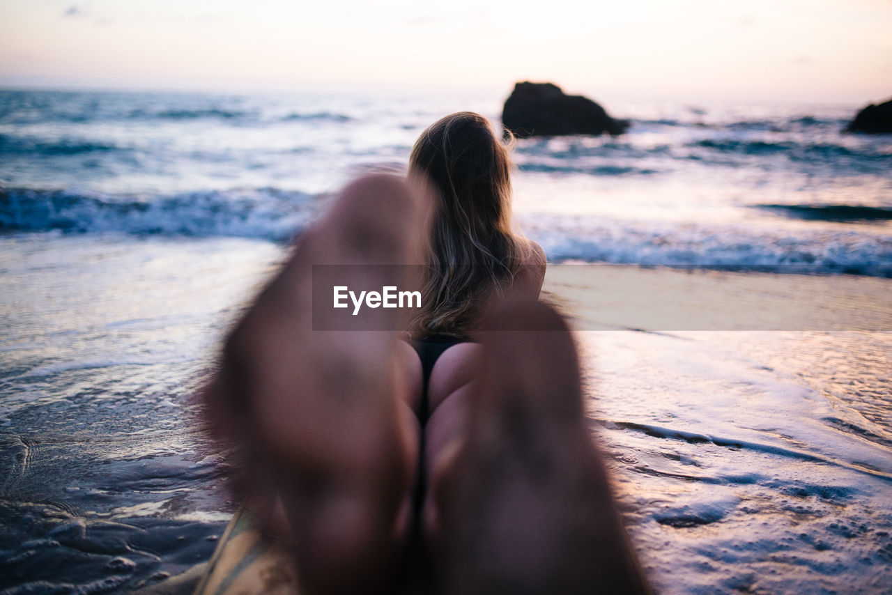 MIDSECTION OF WOMAN AT BEACH AGAINST SKY
