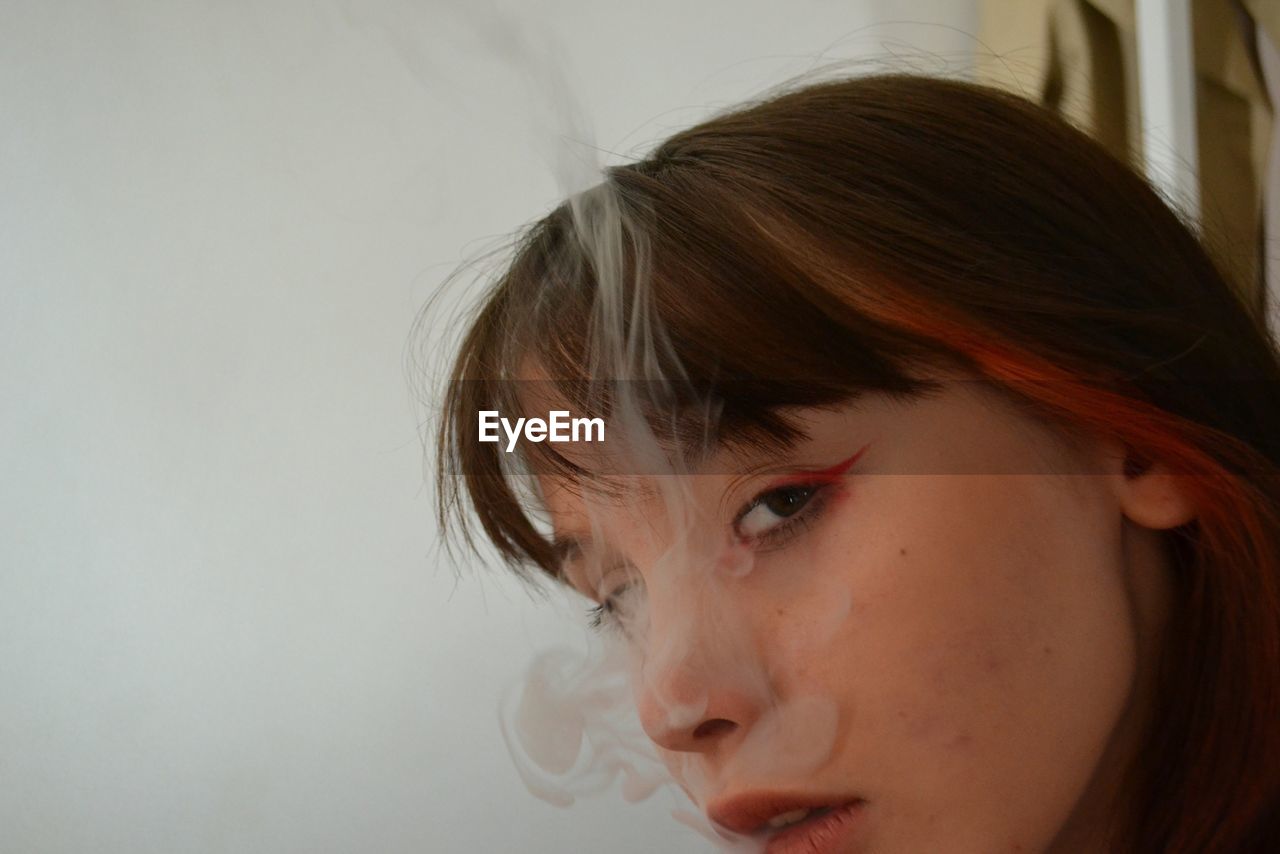 Close-up portrait of woman smoking against white background