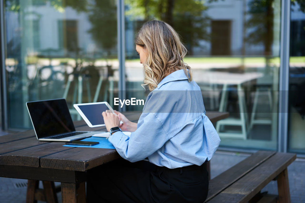 rear view of woman using laptop while sitting on wooden table