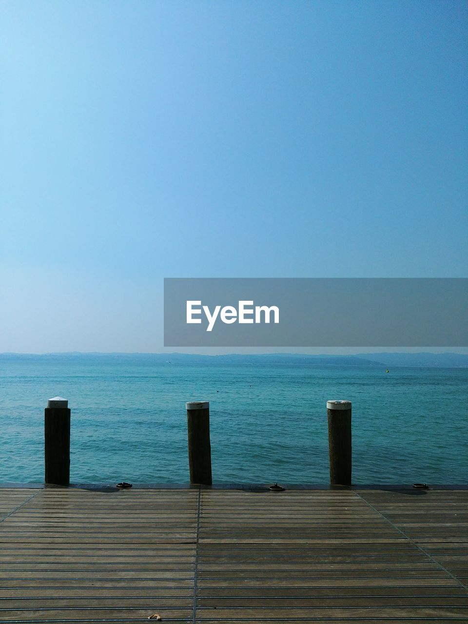 Wooden posts in sea against clear blue sky / serenity / seaside serene view