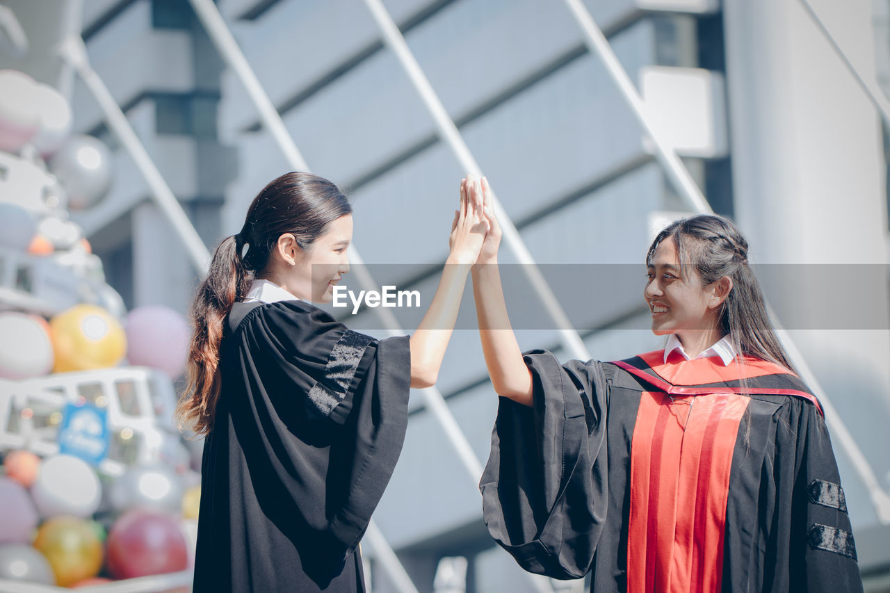 Smiling friends giving high five during graduation