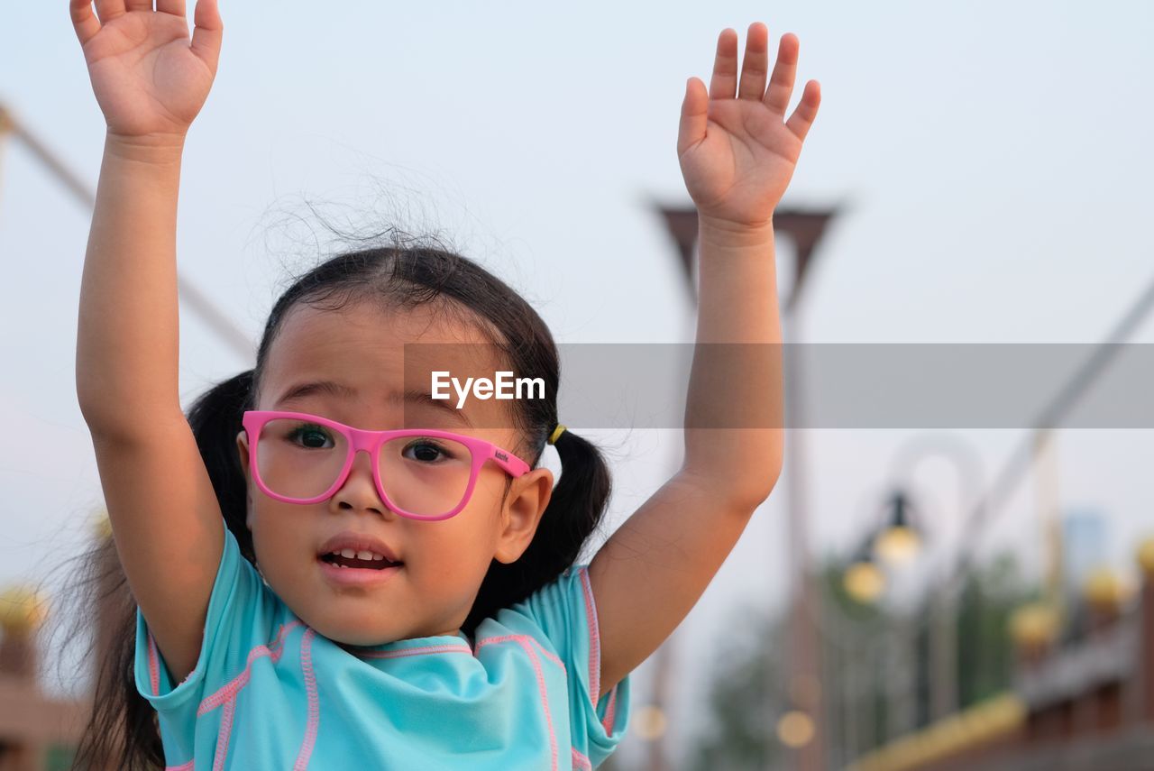 Portrait of cute girl with arms raised on footbridge