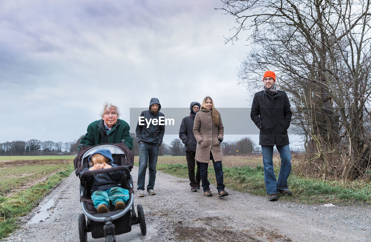 Family on dirt road against sky during winter