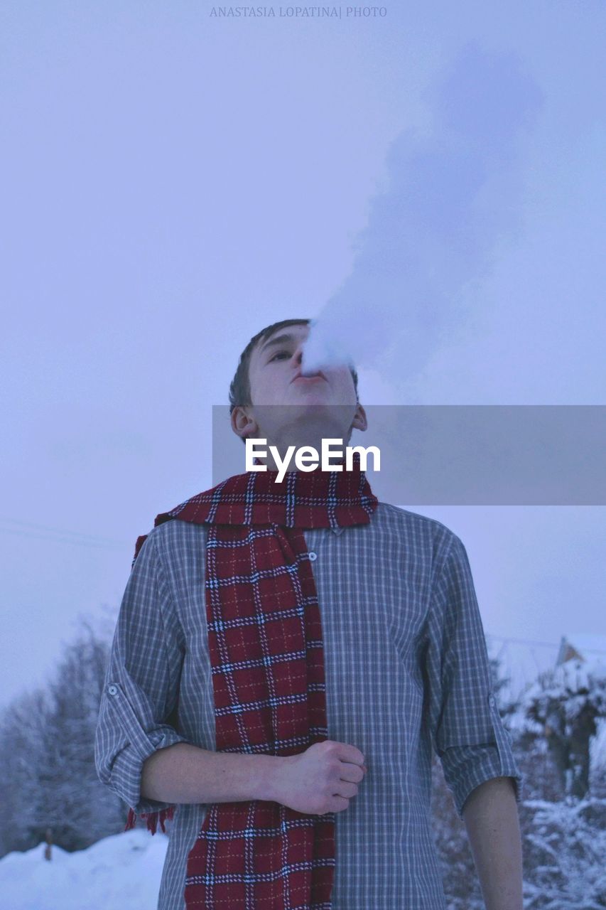 Man smoking cigarette while standing on snow covered field