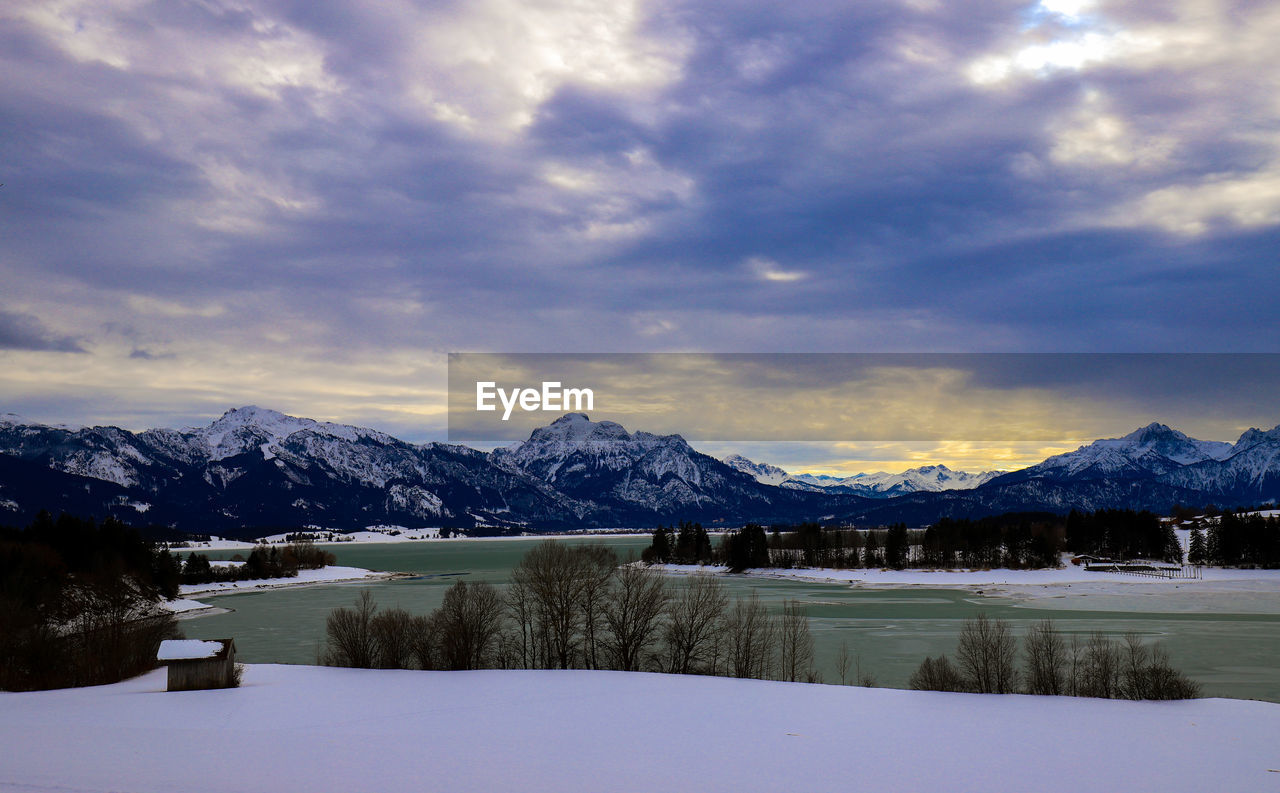 SCENIC VIEW OF LAKE BY SNOWCAPPED MOUNTAINS AGAINST SKY DURING WINTER