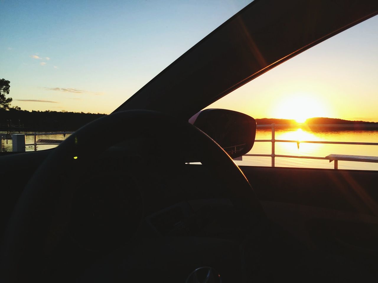 Car by lake against sky during sunset