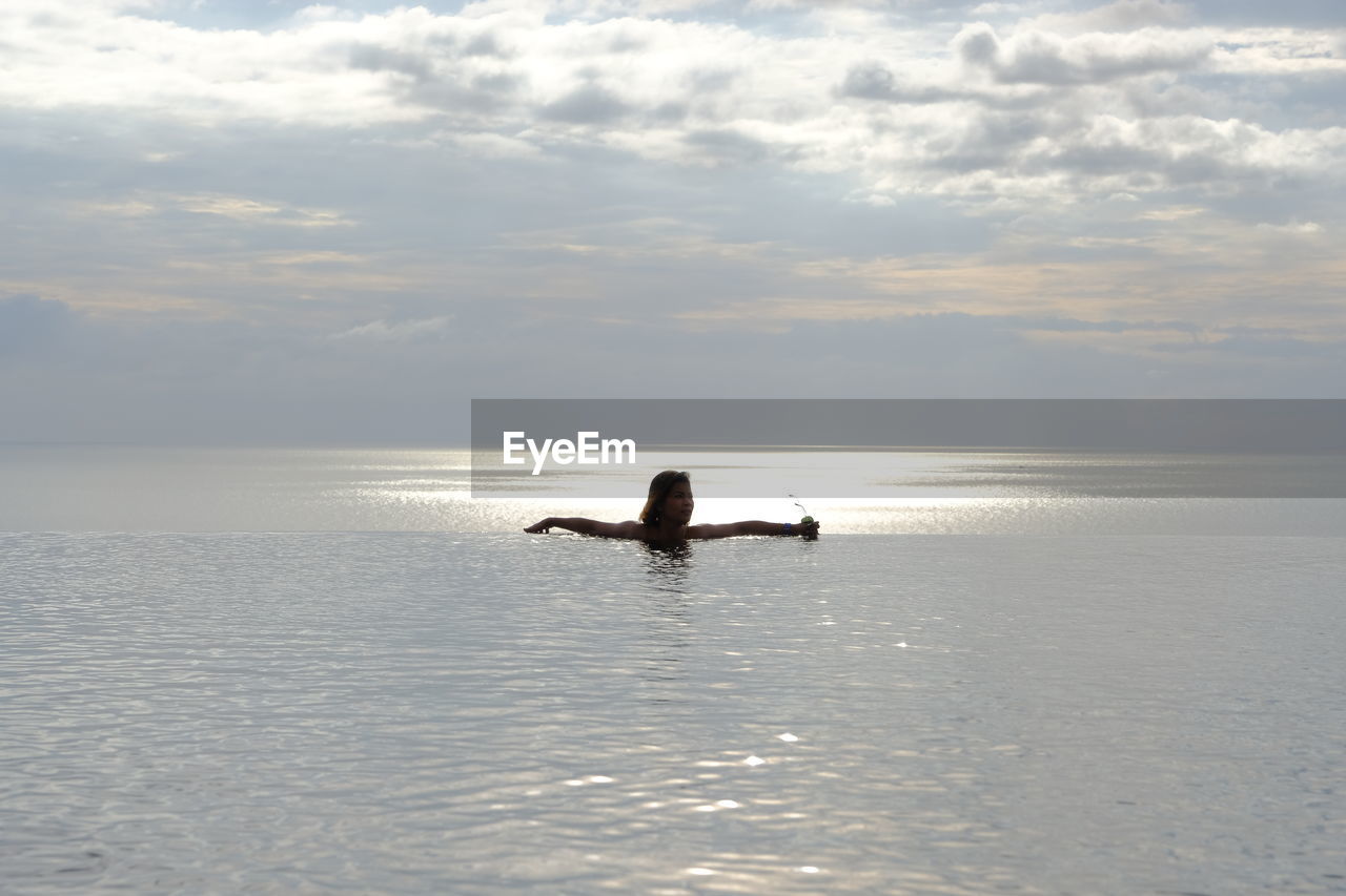 Woman relaxing in infinity pool against sea