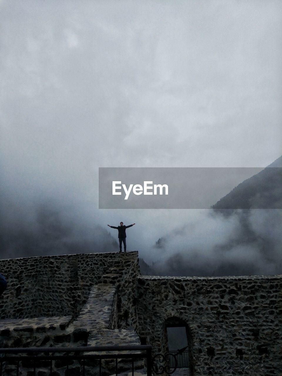 LOW ANGLE VIEW OF MAN STANDING ON BUILDING AGAINST SKY