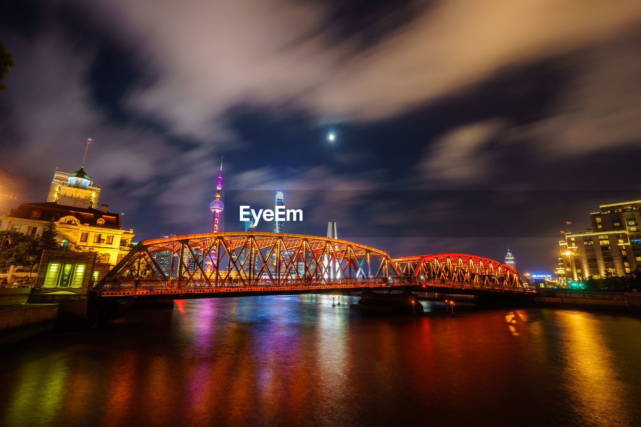 Low angle view of illuminated oriental pearl tower and bridge in front of river against sky in city