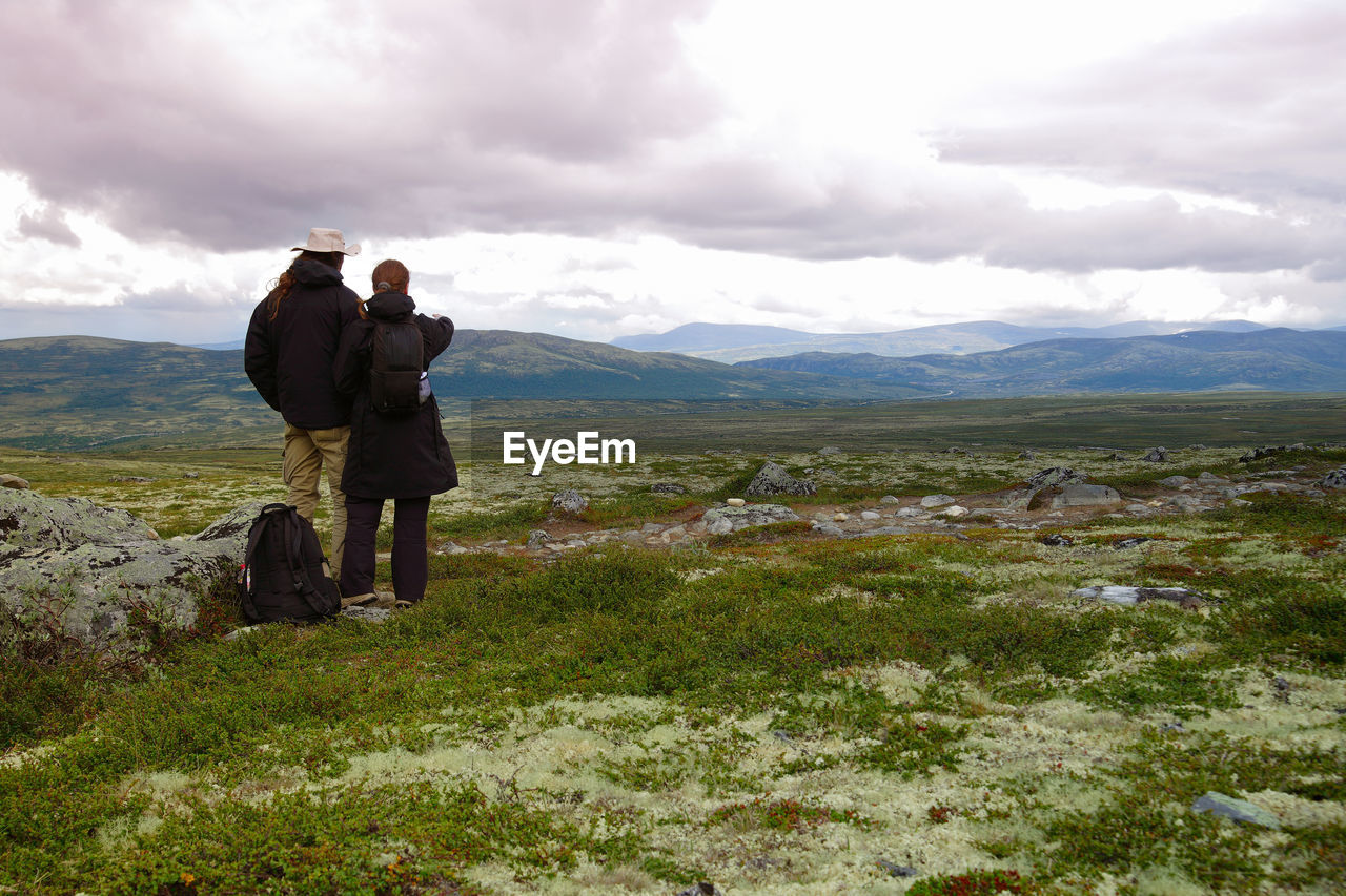 Rear view of friends standing on grassy field at dovrefjellsunndalsfjella national park