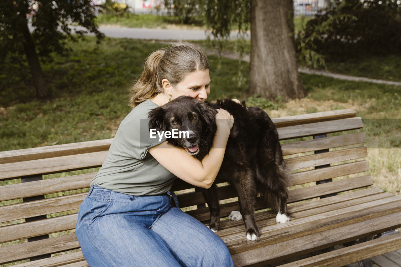 Mature woman embracing dog on bench in park