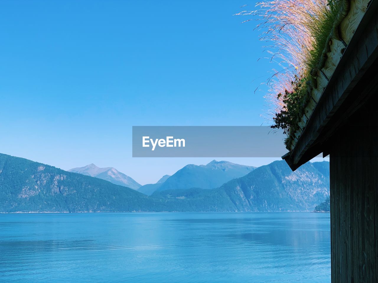 Scenic view of lake and mountains against clear blue sky