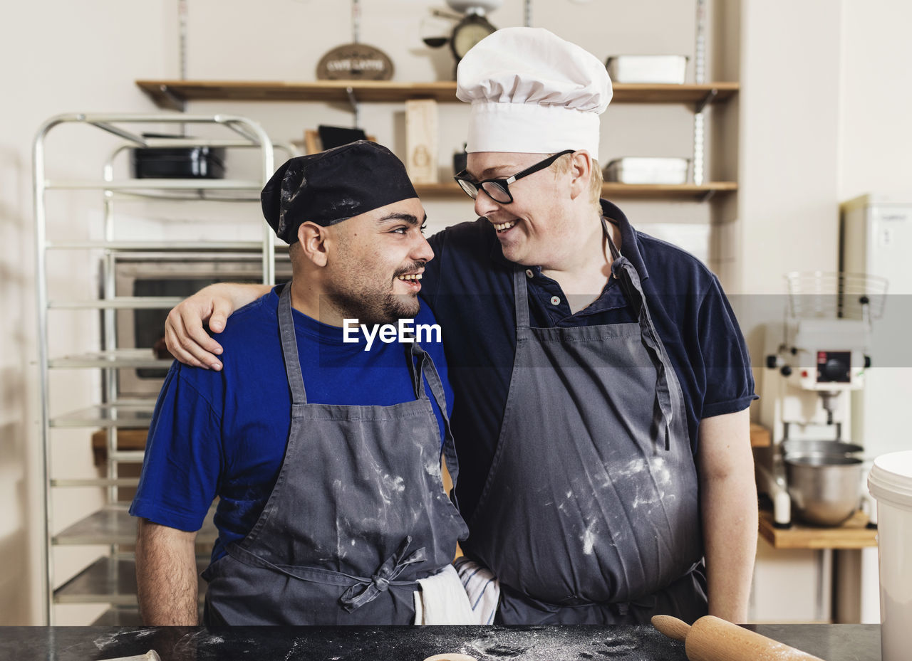 Smiling bakers looking at each other by table in kitchen