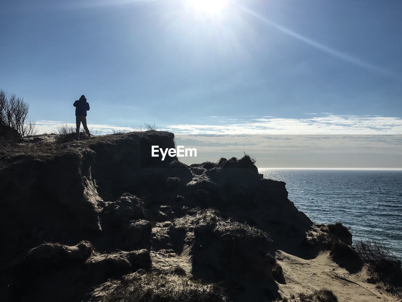 Silhouette person standing on rock at beach against sky during sunny day