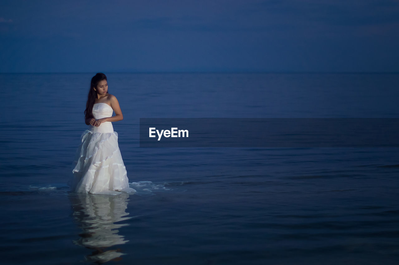 Woman wearing dress while standing in sea at night