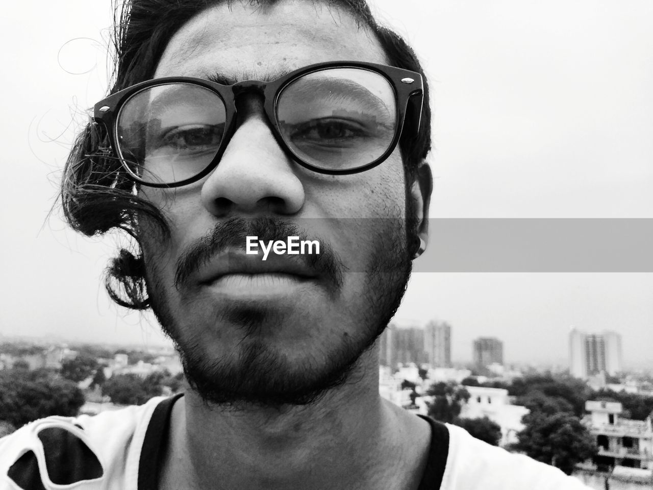 Close-up portrait of serious young man wearing eyeglasses against clear sky