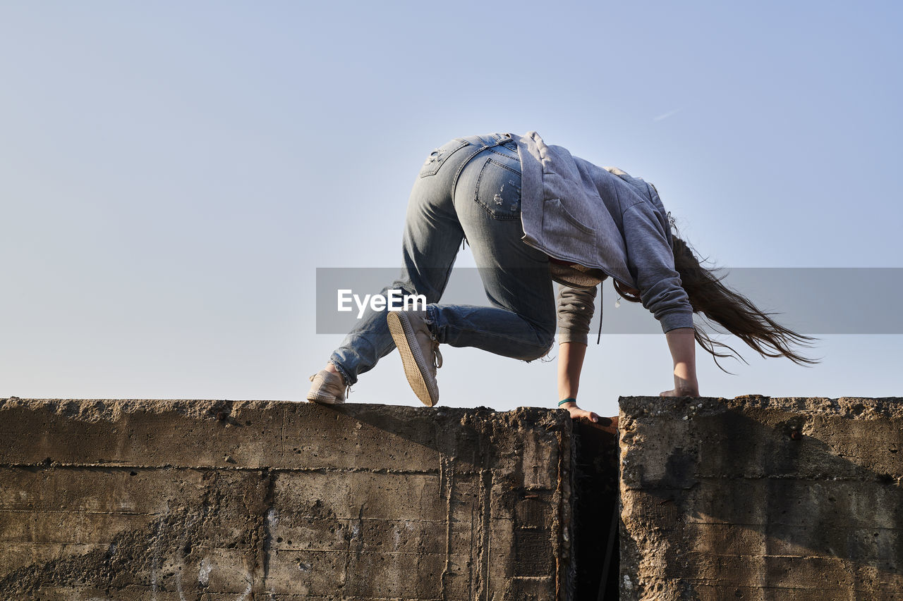 Young woman jumping over concrete wall, rear view