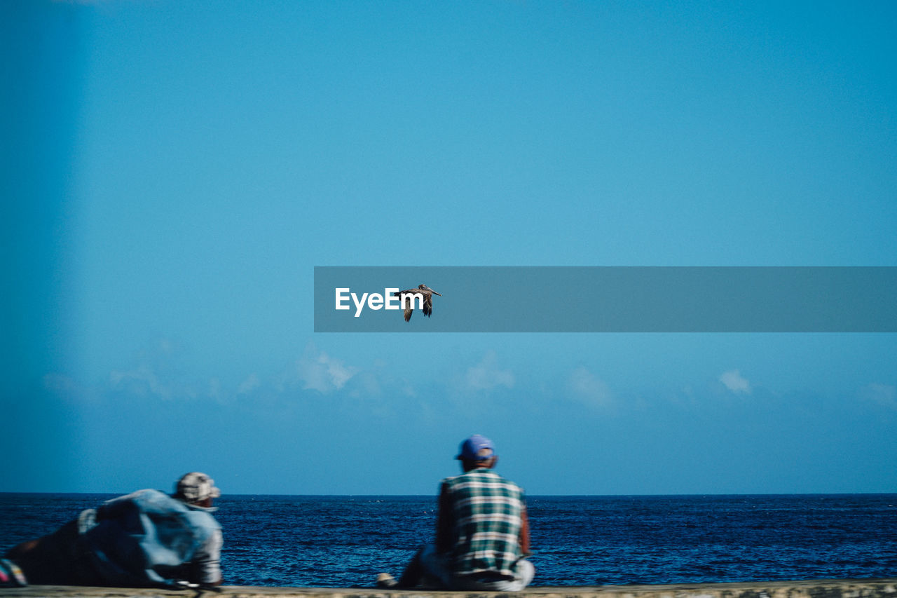 MEN PARAGLIDING IN SEA AGAINST SKY