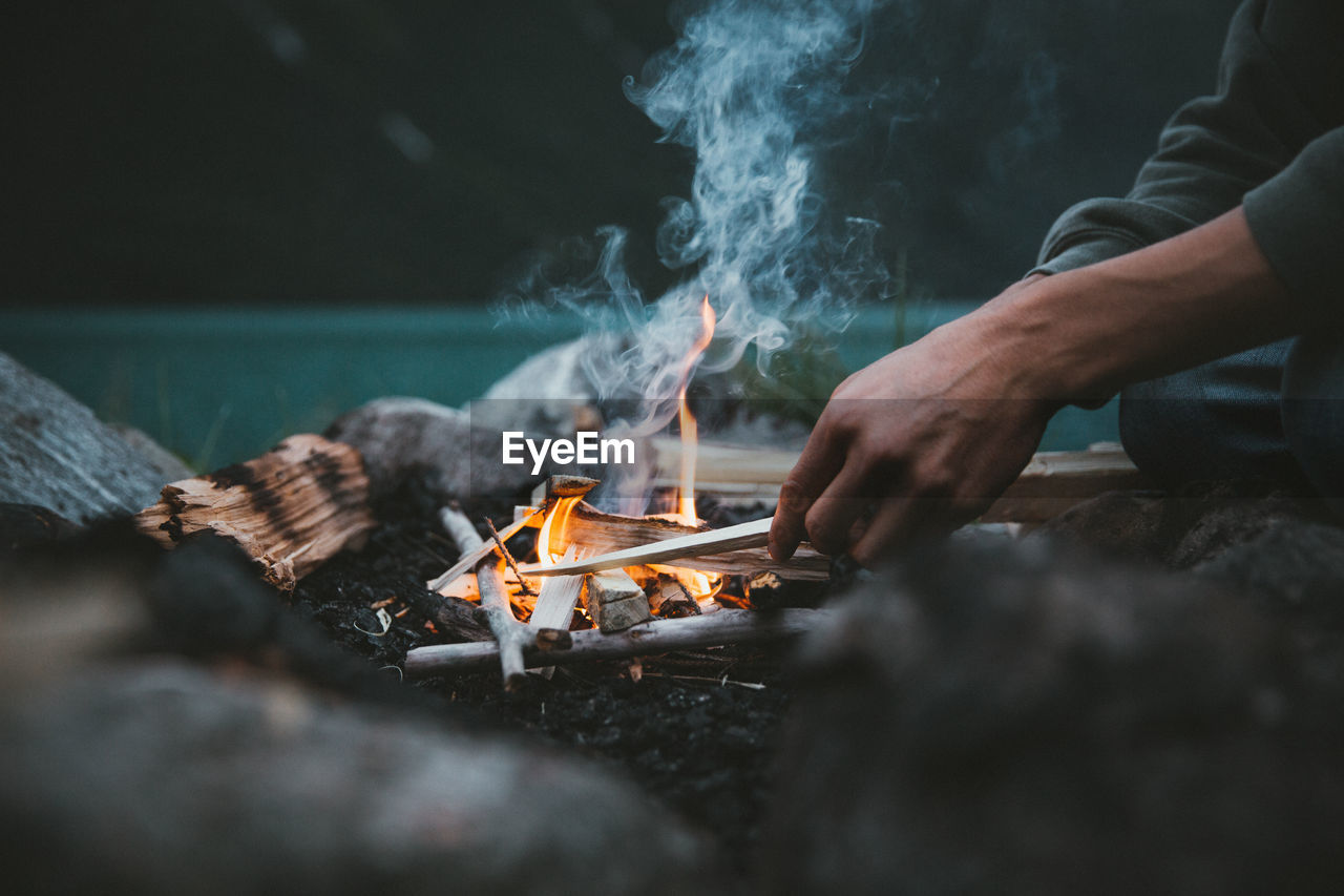 Midsection of man sitting by campfire