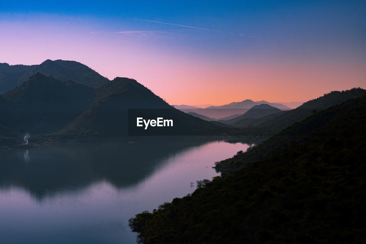 Scenic view of lake and mountains against sky during sunrise