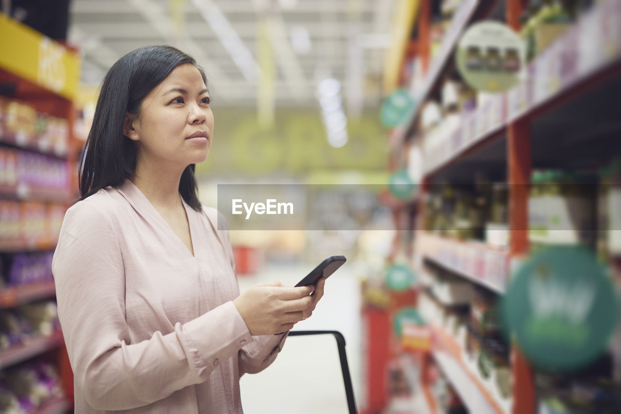 Woman looking at prices during inflation while doing shopping in supermarket