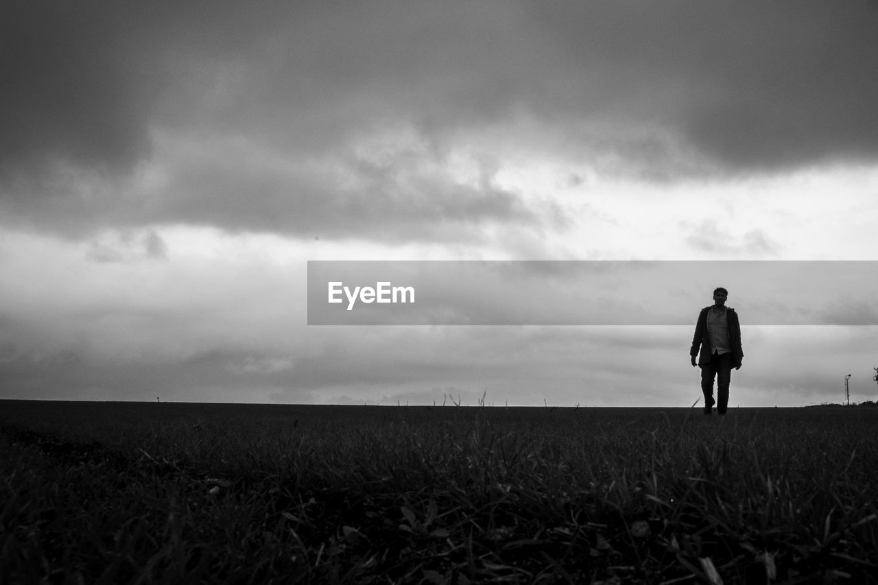 Man walking on land against cloudy sky