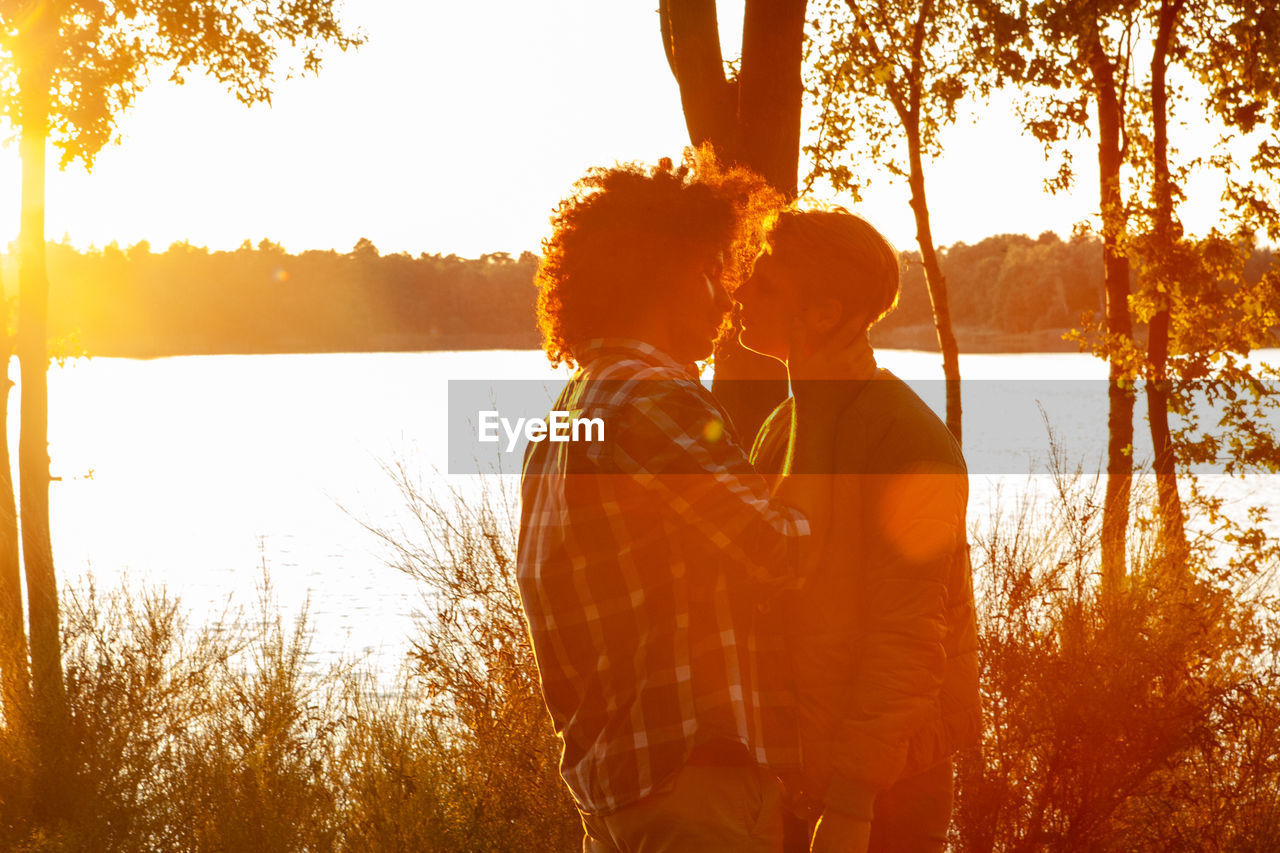 rear view of woman standing by lake against sky during sunset